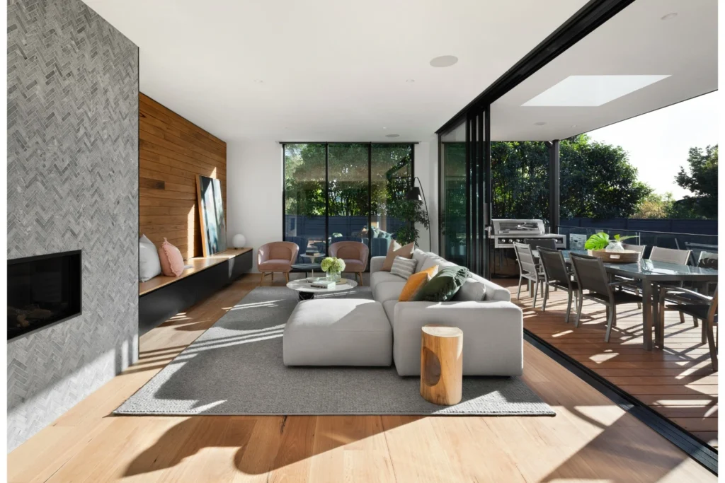 Salon moderne lumineux avec canapé gris, parquet en bois, et vue sur une terrasse extérieure.