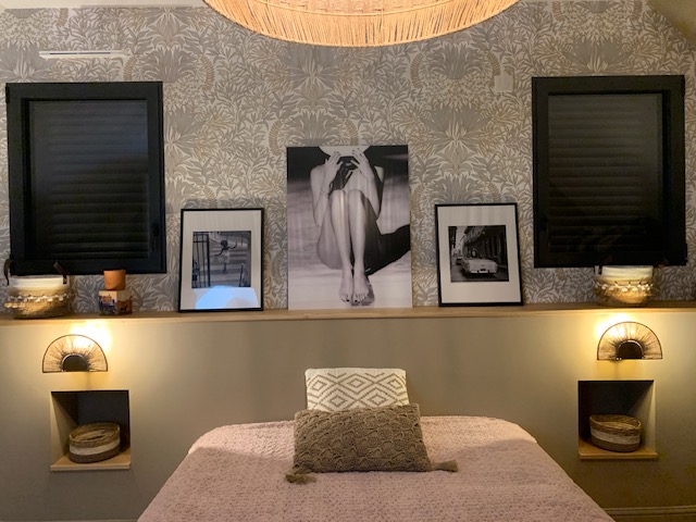 Chambre élégante avec murs en papier peint floral, lit confortable et décoration artistique. Éclairage chaleureux et fenêtres noires.