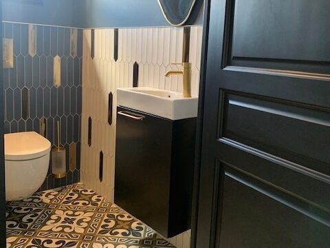Salle de bains moderne avec carrelage graphique, meuble noir et robinet doré. Design soigné et fonctionnalité optimale.
